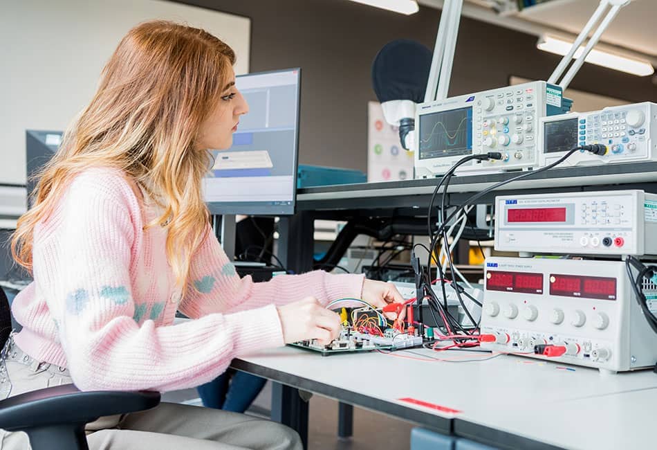 A student testing an electronic circuit board in a lab.