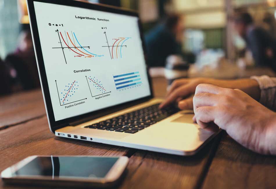 Close up of someone working on a laptop on a table with figures on the screen.