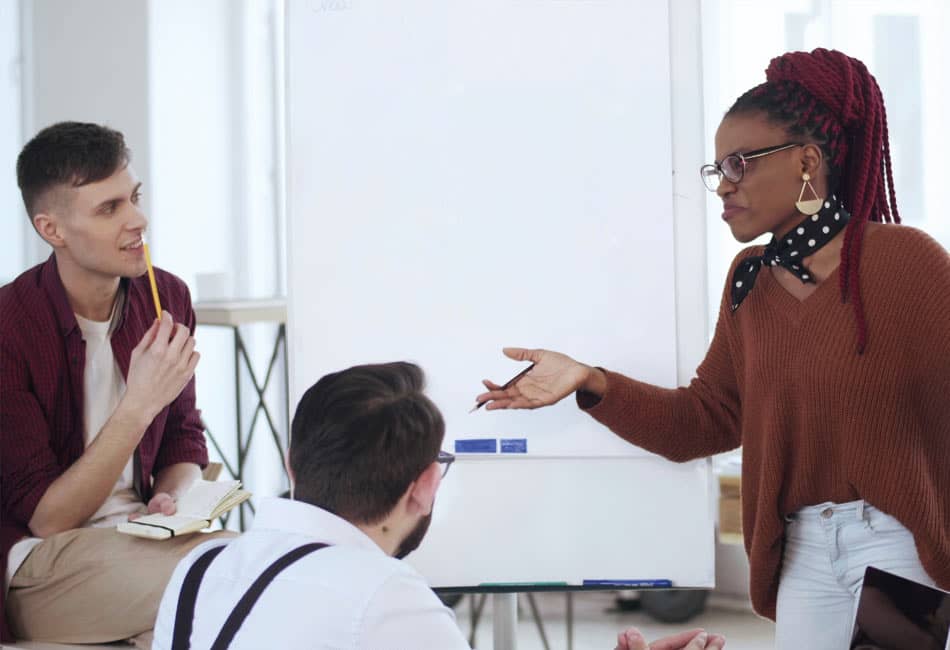 A women talking whilst gesticulating to a couple of men with a clipboard behind her.