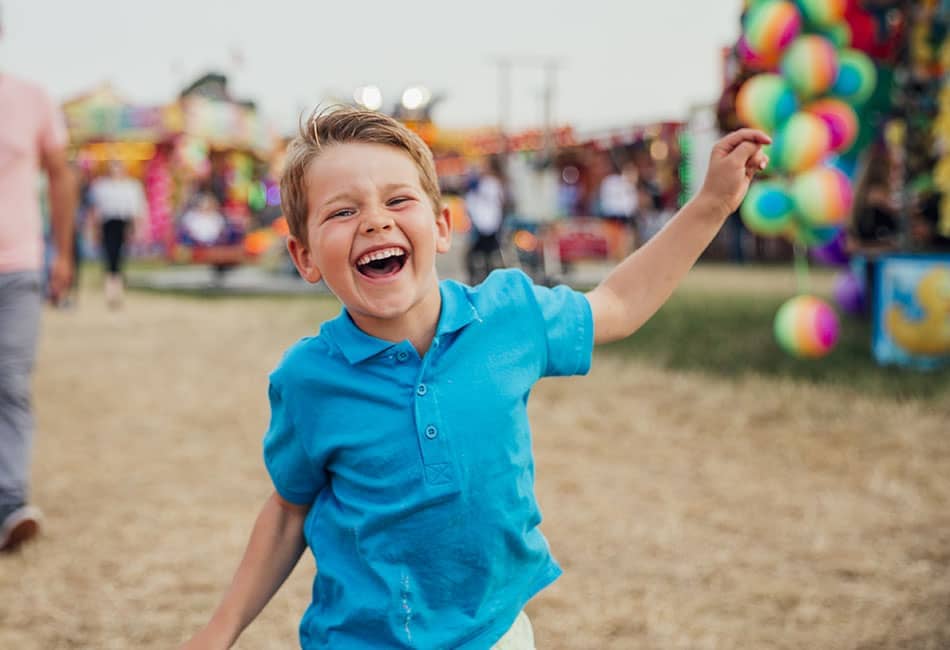 A young boy with a big smile with a fairground in the background.