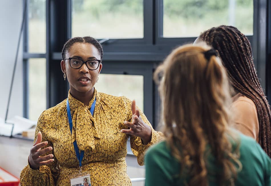 The teacher, a young black woman, is explaining something to two students.