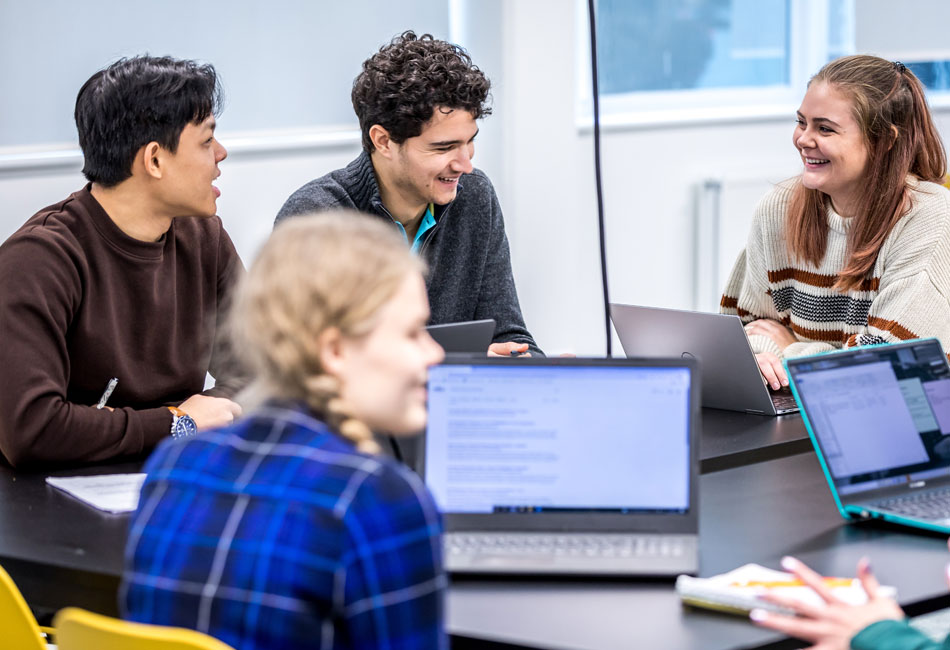 A group students with laptops sat around a table talking to each other.